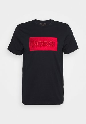 Sort kortærmet t-shirt med rød rektangulær lap på brystet med præget tekst "KORS".