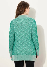 Long cardigan tricoté vert avec un motif en vagues, des poignets et un ourlet côtelés. La texture est légère avec une coupe décontractée.