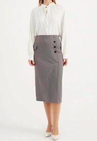 Weiße Bluse mit langen Ärmeln und Rüschenausschnitt, kombiniert mit einem grauen Bleistiftrock mit Nadelstreifen, der eine Seitentasche und schwarze Knöpfe hat.