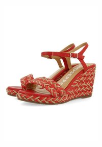 Sandalias rojas de cuña con detalles de paja trenzada, correas para el tobillo y un interior suave. La suela texturizada ofrece estabilidad.