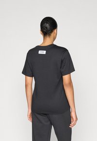 Černé bavlněné tričko s kulatým výstřihem a krátkými rukávy, s bílou etiketu značky na horní části zad. Hladká textura.