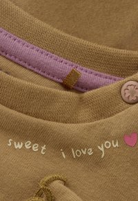 Bruine stof met een zachte textuur, met roze stiksels, een knop en gedrukt tekst: "sweet i love you" met een klein hartpictogram.