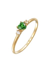 Bague en or avec une pierre précieuse verte en forme de cœur au centre, flanquée de deux petites pierres claires, le tout sur une bande lisse et fine. Poinçon en argent visible.