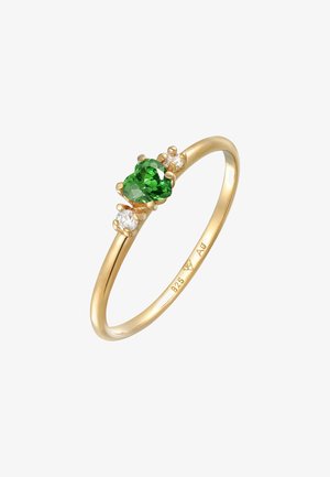 Bague en or avec une pierre précieuse verte en forme de cœur au centre, flanquée de deux petites pierres claires, le tout sur une bande lisse et fine. Poinçon en argent visible.
