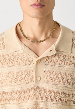 Beige knitted polo shirt featuring a lace-like pattern, short collar, three buttons, and a gold chain necklace.