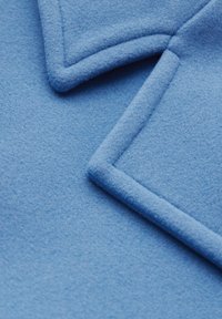 Tessuto in pile di colore azzurro chiaro con una superficie testurizzata, caratterizzato da bordi piegati e cucitureaccurate per un design strutturato.