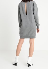 Vestido sudadera gris con corte en la espalda, mangas largas y dobladillo acanalado, combinado con botas blancas hasta el tobillo. Textura de tela suave.