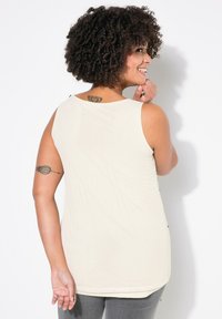 Beige tank top with a scoop neckline and a relaxed fit. The fabric has a soft texture. It features an accent design on the back.