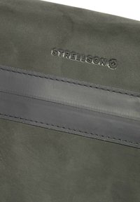 Szary zamszowy materiał z ciemniejszym szarym paskiem i wytłoczonym logo "Strellson". Gładka faktura z starannym przeszyciem wzdłuż szwu.