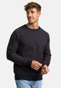 Pull marine avec un motif géométrique en losanges, tissu texturé, poignets et ourlet côtelés, encolure ronde. Coupe décontractée ; idéal pour le superposition.