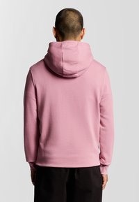Felpa rosa con una texture morbida, un fit rilassato e un grande cappuccio. I polsini e l'orlo sono costolati, senza loghi o motivi visibili.
