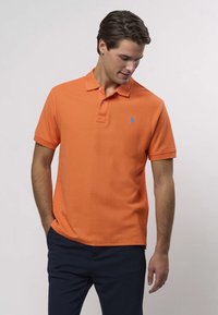 Oranžist polo-särk, mis on valmistatud tekstureeritud kangast, klassikalise krae, kolme nupuga esiosaga ja väikese sinise logoga rinnal.