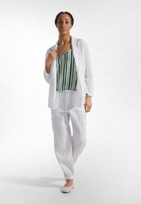 Biała lniana marynarka o luźnym kroju, zielono-niebieski paskowany top, białe lniane spodnie z elastycznymi mankietami oraz lekkie baleriny.