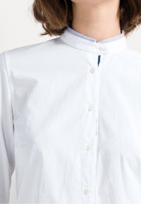 Bílé košilové tričko s vysokým límečkem, modrou vzorovanou lemovkou, předním knoflíkovým zapínáním a měkkým bavlněným materiálem.