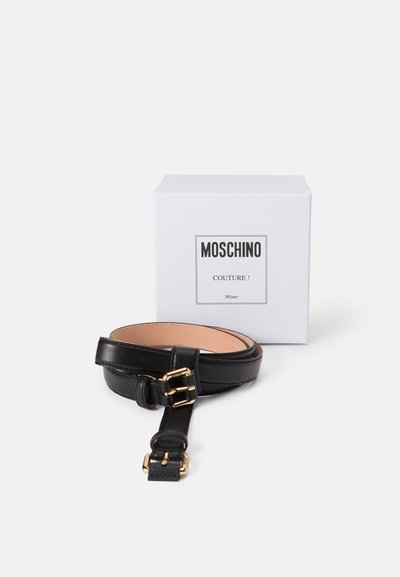 Cinturón de cuero negro con textura suave, con hebilla dorada y acentos. Presentado junto a una caja blanca con la etiqueta "¡Moschino Couture!".