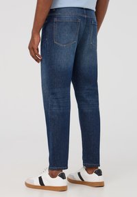 Jeans blu scuro in denim, con vestibilità dritta, design a cinque tasche e cuciture a contrasto. Abbinati a sneaker bianche.