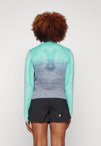 Langærmet sports top i teal og grå gradient, med en tætsiddende pasform og rund halsudskæring, parret med sorte shorts.