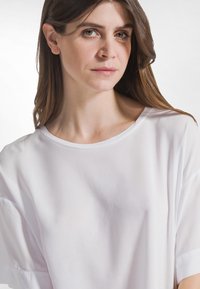 Witte top met korte mouwen van gladde stof, met een brede halslijn en een losse pasvorm, voorzien van een subtiele glans en een zachte textuur.