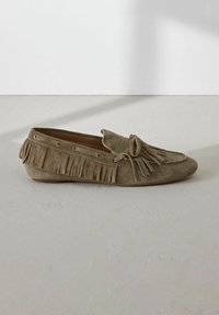 Mocasín de ante gris con detalles de flecos, acento de lazo y cordones laterales. Presenta una suela plana, textura suave y diseño de punta redondeada.