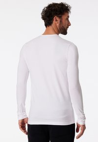 T-shirt bianco a maniche lunghe in tessuto morbido e elasticizzato con scollatura rotonda. Spalle senza cuciture, texture liscia, silhouette aderente.