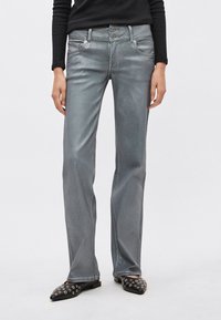 Metallist hõbedased teksad kitsama lõikega, kahe lukuga, esitaskutega ja kerge läikega. Ühendatud mustade kaunistustega libisevate jalanõudega.