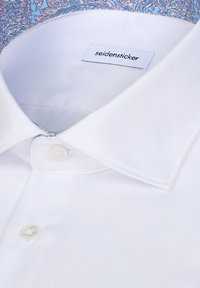 Col de chemise blanche à boutons, avec une étiquette indiquant "seidensticker" et une doublure intérieure bleue à motif.