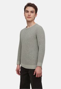 Helles graues Strickpullover mit einem strukturierten Muster, Rundhalsausschnitt und gerippten Bündchen. Der Körper ist leicht lässig geschnitten und wird mit dunklen Hosen kombiniert.