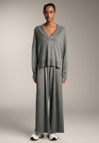 Maglione grigio a maglia con colletto a scialle e maniche ampie, abbinato a pantaloni a gamba larga coordinati. Texture liscia e vestibilità rilassata.