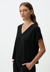 Blusa nera a maniche corte con scollatura a V. Realizzata in tessuto morbido, presenta una vestibilità rilassata e spacchi laterali per facilitare i movimenti.