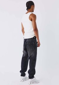 Canotta bianca, jeans scuri in denim e sneakers bianche. I jeans hanno una texture scolorita e due tasche posteriori, con una vestibilità comoda.