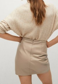 Beige geribbelde trui met oversized mouwen, gecombineerd met een aansluitende beige leren minirok met een rits aan de achterkant en een soepele textuur.
