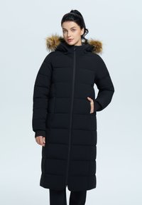 Schwarze Steppjacke mit Kapuze, die einen Kunstfellbesatz hat, gesteppter Optik, langer Länge und Seitentaschen. Reißverschluss vorne.