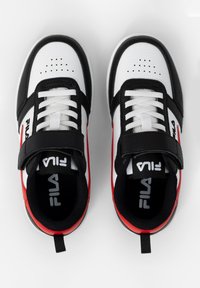 Valkoiset, mustat ja punaiset FILA-tennarit nauhoilla ja tarranauhoilla, nähtynä ylhäältä valkoista taustaa vasten.