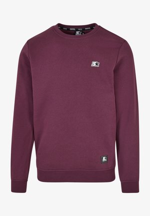 Bordo spalvos megztinis su ilgomis rankovėmis, apvaliu kaklu ir raukšlėmis ant rankovių. Yra mažas logotipas krūtinėje ir audinys ant apvado.