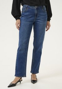 Mėlynos džinsinės kelnės su tiesiu pjūviu, penkiomis kišenėmis ir auksinėmis siūlėmis. Papildytos juodais smailiais aukštakulniais.