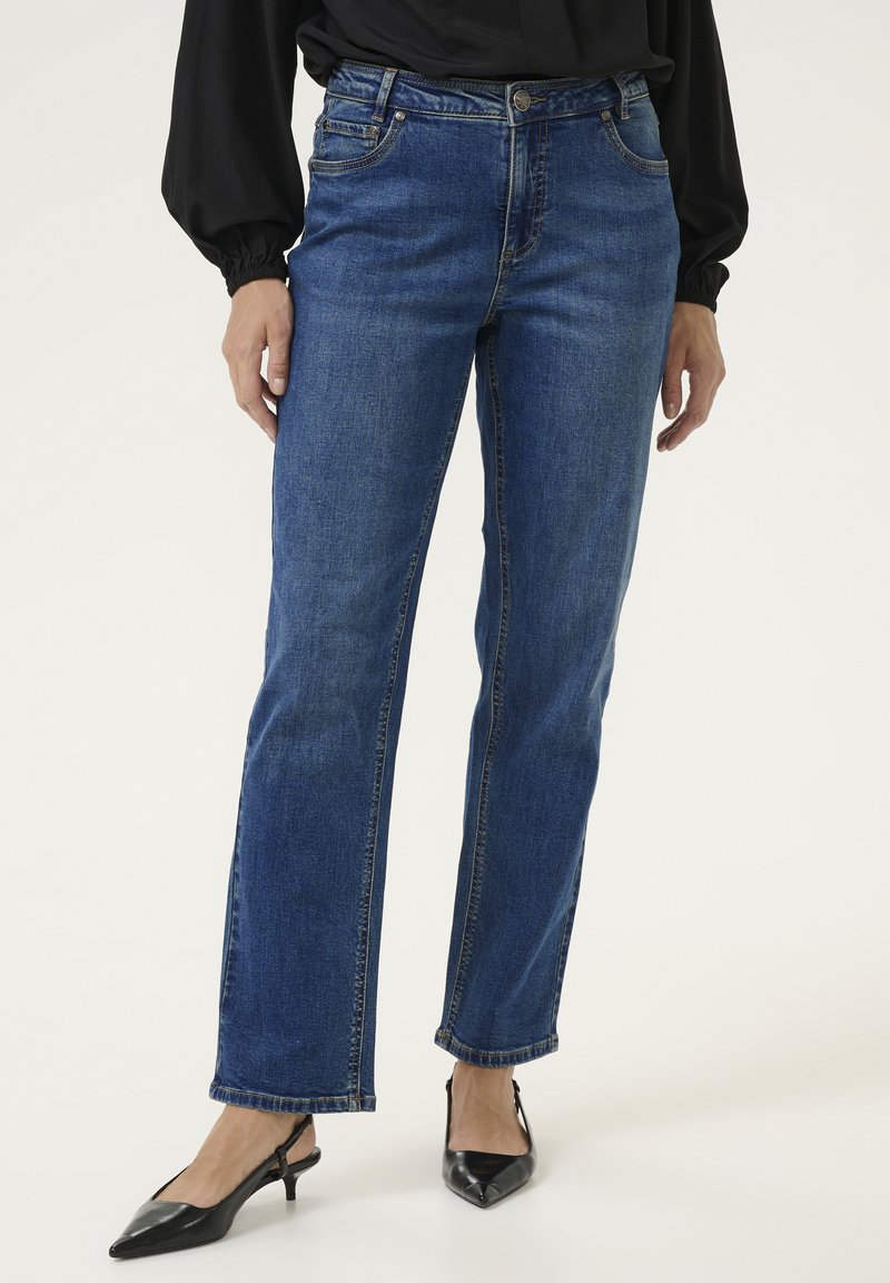 Mėlynos džinsinės kelnės su tiesiu pjūviu, penkiomis kišenėmis ir auksinėmis siūlėmis. Papildytos juodais smailiais aukštakulniais.