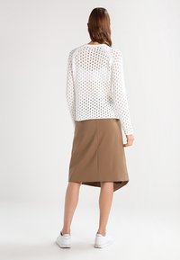 Haut à manches longues perforé blanc associé à une jupe marron à mi-mollet. Des baskets blanches complètent le look. Texture lisse avec une coupe décontractée.