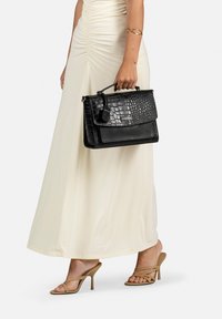 Borsa nera in pelle con effetto coccodrillo, dalla forma strutturata, con manico superiore e chiusura a scatto. Arricchita da un'etichetta con logo e dettagli in pelle liscia.