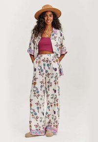 Květinový outfit s krátkým rukávem, otevřenou bundou a kalhotami širokého střihu. Barvy zahrnují bílou, modrou, růžovou a přírodní odstíny. Doplněno béžovým kloboukem.