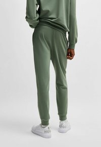 Groene joggingsbroek met een gladde textuur, elastische tailleband, zijzakken en geribde boorden, gecombineerd met witte sneakers met logodetails.