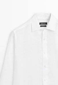 Chemise blanche à manches longues avec col pointu, boutons visibles et étiquette noire lisant "Massimo Dutti 100 % lin" à l'intérieur du col.