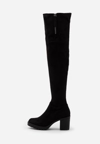 Botas negras sobre la rodilla, hechas de suave ante, con un tacón grueso y cremallera lateral para facilitar su uso. Presentan una textura suave y punta redonda.