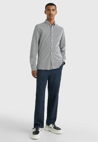 Camisa de botón a rayas en blanco y marino, combinada con pantalones marinos y zapatillas en blanco y negro. Corte slim con mangas largas y cuello.