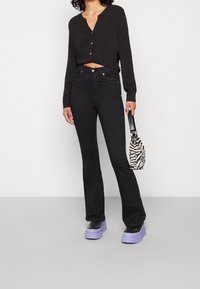 Top negro ajustado de manga larga con botones, jeans negros de campana, zapatos de plataforma negros con suelas moradas y un bolso de print de cebra.
