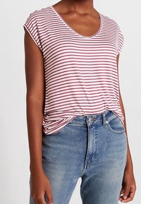 Pruhované tričko v světle růžové a burgundské barvě s krátkými rukávy a kulatým výstřihem; nošeno přes světle modré džíny s mírně vybledlým povrchem.