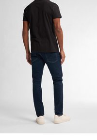 Černé triko s krátkým rukávem, tmavě modré džíny se světlým švem a krémové tenisky. Jednoduchý design; volný střih, bez viditelných vzorů.