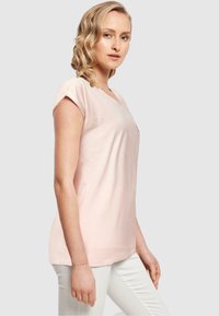 Lyserød kortærmet V-hals t-shirt i blødt bomuld. Enkel design med en afslappet pasform, båret med hvide bukser. Ingen synlige mønstre.