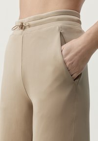 Beige, hoge taillebroek van soepel stof met een aantrekkoord en zijzakken. Slanke pasvorm met stikdetails langs de naden.