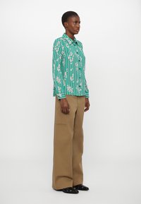 Green striped shirt with floral pattern, collared design. Paired with tan wide-leg pants, featuring side pockets and black shoes.