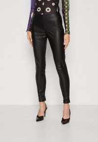 Pantaloni neri in finta pelle a vita alta, con una vestibilità slim, texture liscia e design alla caviglia. Indossati con scarpe con tacco nere.